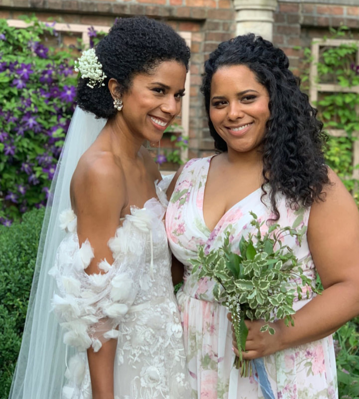 Black bride in white floral lace dress with maid of honor in garden