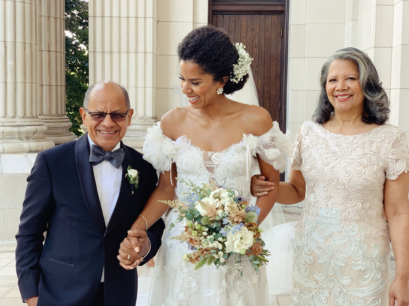 Black bride with updo hair style and bouquet walking with parents at wedding